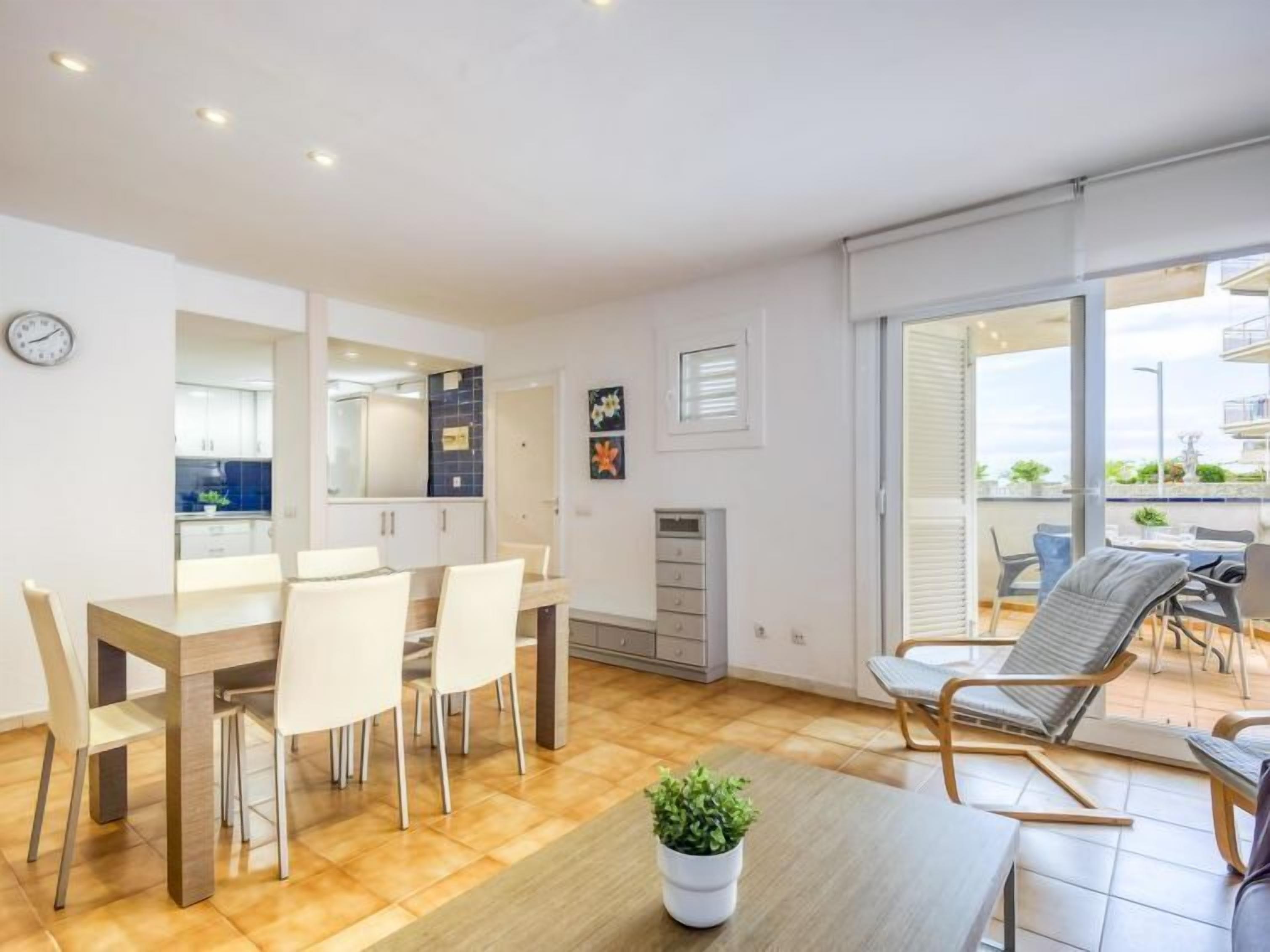 Een moderne keuken met witte kasten, een eethoek met een houten tafel en stoelen, en een balkon met buitenmeubels.