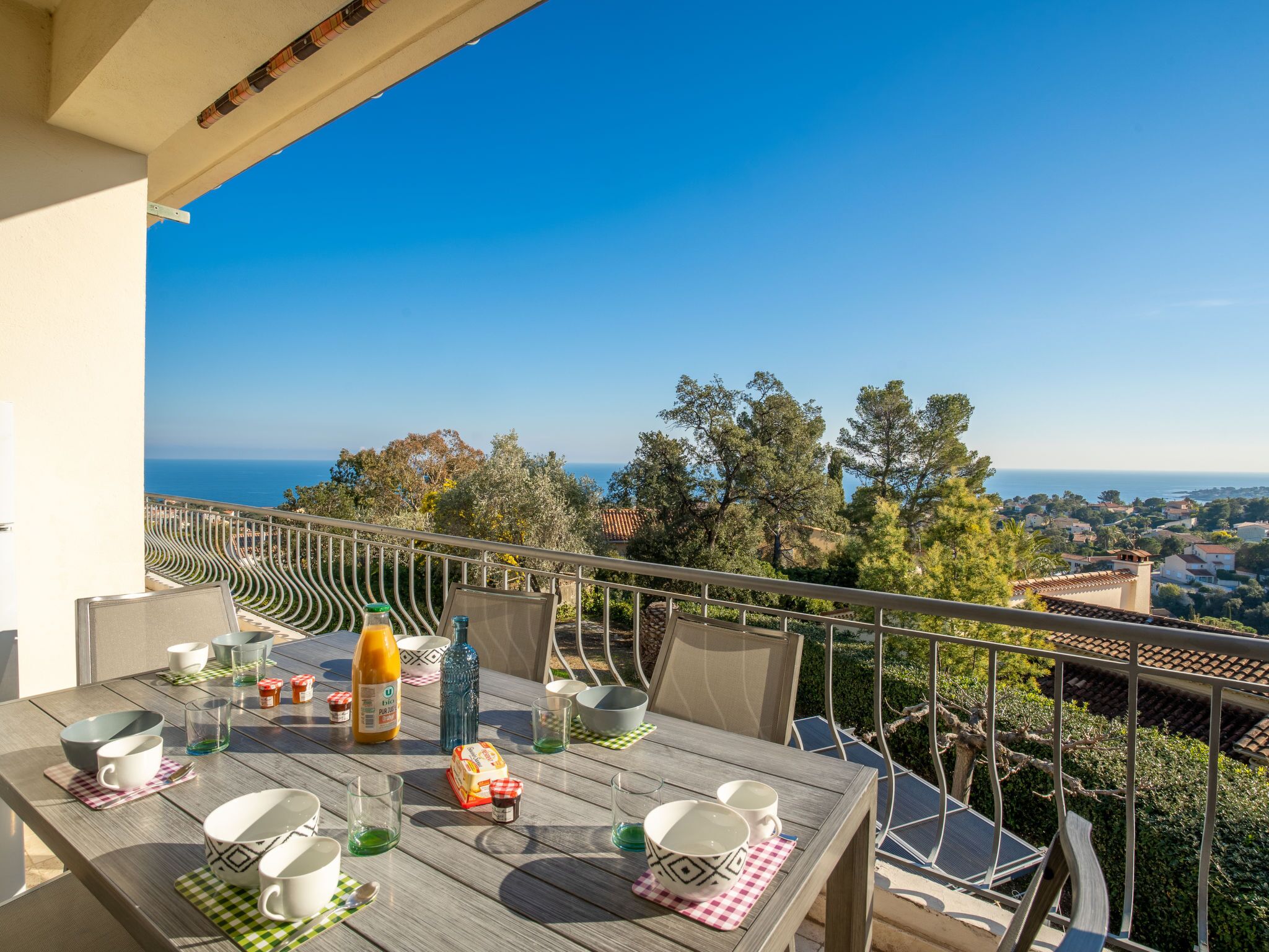 A balcony with a table set for dining, overlooking a scenic view of the sea and surrounding landscape.