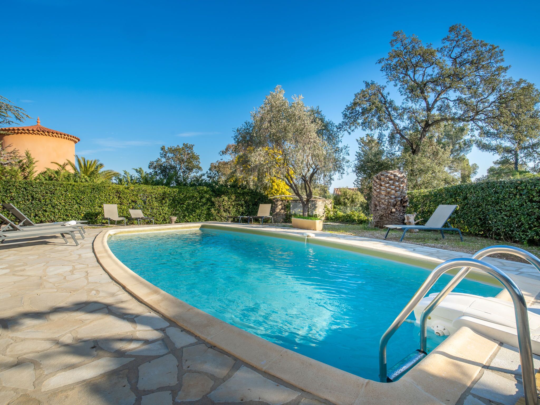 A clear blue swimming pool with lounge chairs and a stone pathway.