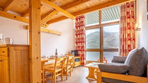 A wooden interior with a dining area, a sofa, and a large window with curtains. - Brelin Danchet 1026 by Interhome (Les Menuires)