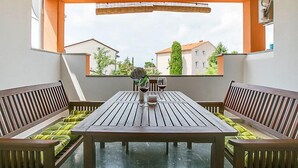 Ein Balkon mit Holztisch und Bänken, einem Blumentopf und Blick auf Gebäude.