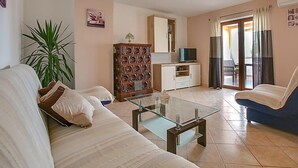 Ein Wohnzimmer mit einer Couch, einem Glastisch, einem Schrank und einem Fernseher.