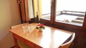 Ein Holztisch mit drei Weingläsern und einer Weinflasche, einer kleinen Topfpflanze und einem Fenster mit Blick auf einen Balkon.