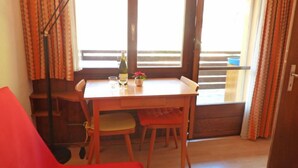 Ein Zimmer mit einem Holztisch, zwei Stühlen, einem roten Sofa, einer Stehlampe und einem Fenster mit Vorhängen.