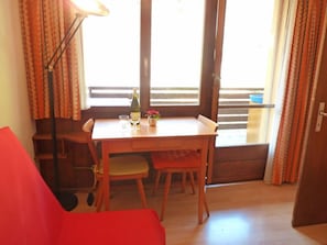 Une pièce avec une table en bois, deux chaises, un canapé rouge, un lampadaire et une fenêtre avec des rideaux.