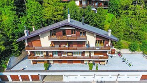 Ein mehrstöckiges Gebäude mit Balkonen, einer flachen Dachterrasse und einem umgebenden Wald.