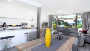Una sala de estar moderna con comedor, cocina y un amplio ventanal corredero que da a un balcón.