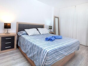 A neatly made bed with striped bedding, a bedside lamp, and a folded towel on the bed. - Cap Roig by Interhome (St Antoni de Calonge)
