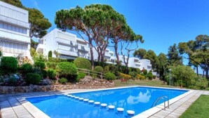 Una piscina con borde de baldosas, rodeada de follaje cuidado y edificios blancos.