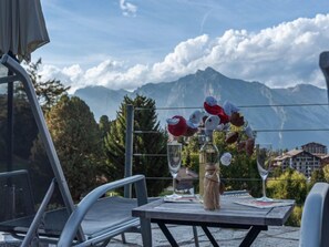 A table with a vase of flowers and wine glasses, overlooking a mountainous landscape. - Chalet Aquarius by Interhome (Nendaz)