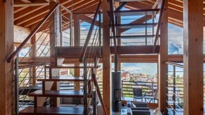 Un interior espacioso con una escalera de madera, ventanas amplias que ofrecen vistas al exterior y una chimenea.
