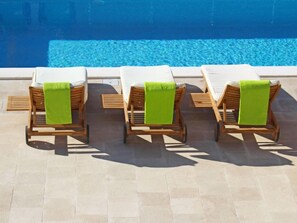 Tres sillas de madera con toallas verdes, dispuestas en fila junto a una piscina.