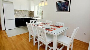 Et moderne køkken med hvide skabe, en sort bordplade og et spiseområde med et glasbord og hvide stole.