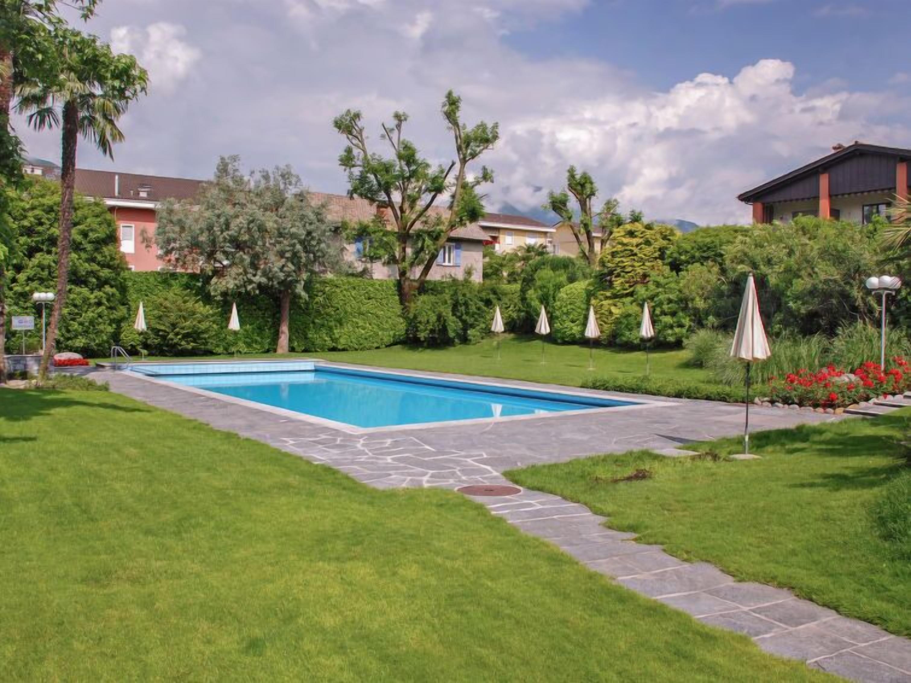 A rectangular swimming pool with a stone border, surrounded by well-maintained grass and hedges.