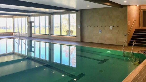 Ein Innenpool mit großen Glaswänden, Holzboden und einer Treppe, die zu einer erhöhten Ebene führt.