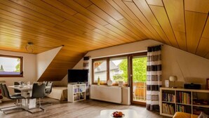 Ein gemütliches Dachzimmer mit Essbereich, Fernseher und Bücherregal.