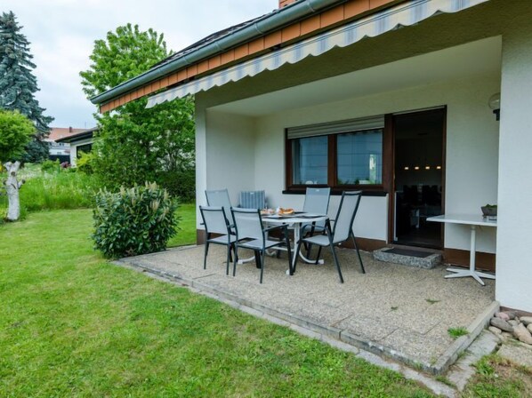 A covered patio with a table and chairs, a window, and a door leading to an interior space.