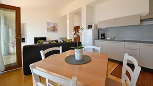 Une cuisine moderne avec des meubles blancs, une table à manger avec des chaises et un petit îlot central agrémenté d’une plante.