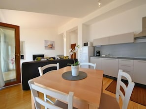 Cozinha moderna com armários brancos, uma mesa de jantar com cadeiras e uma pequena ilha com uma planta.