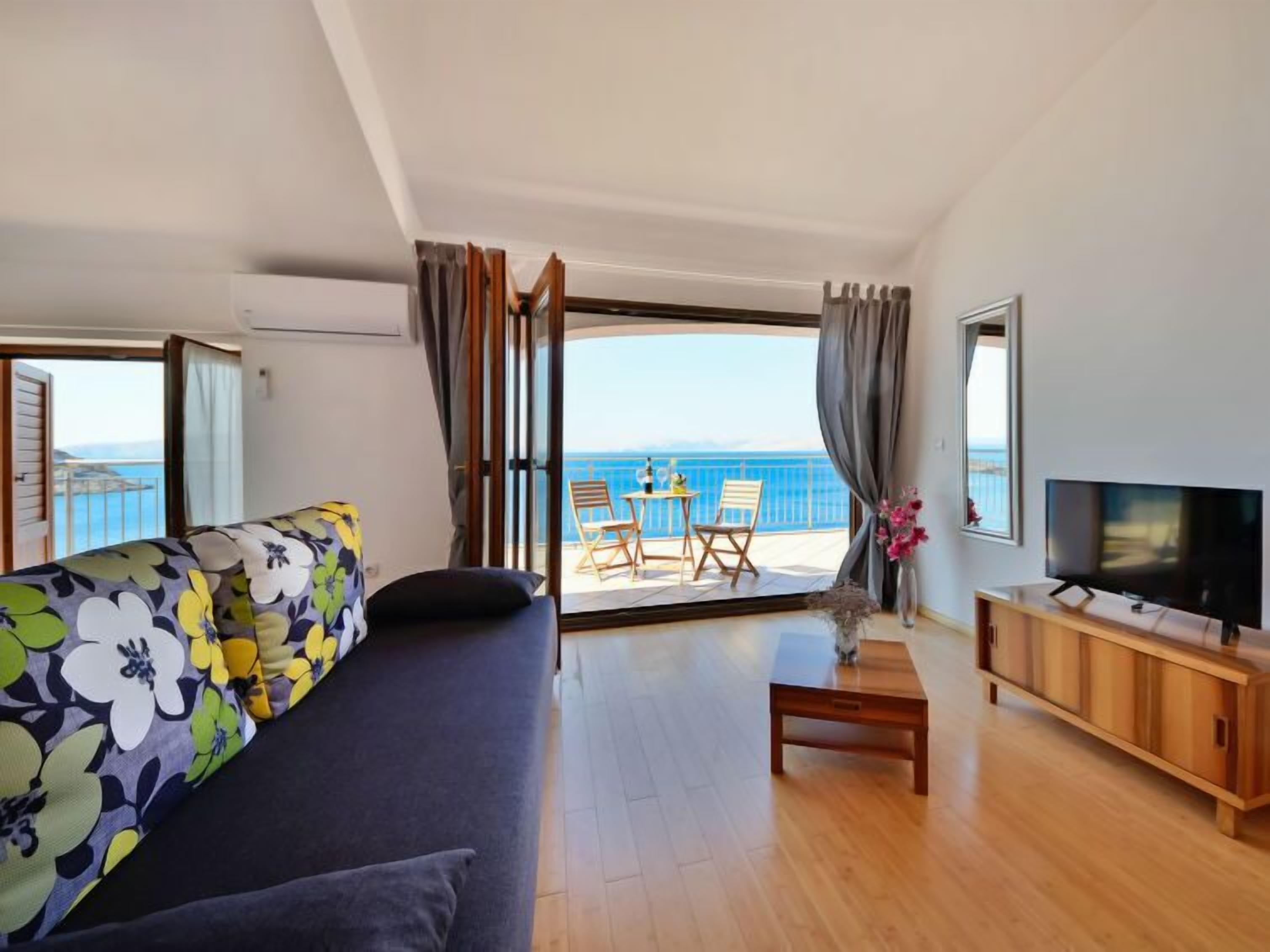 A modern living room with a sofa, a TV, a wooden coffee table, and a balcony with a table and chairs.