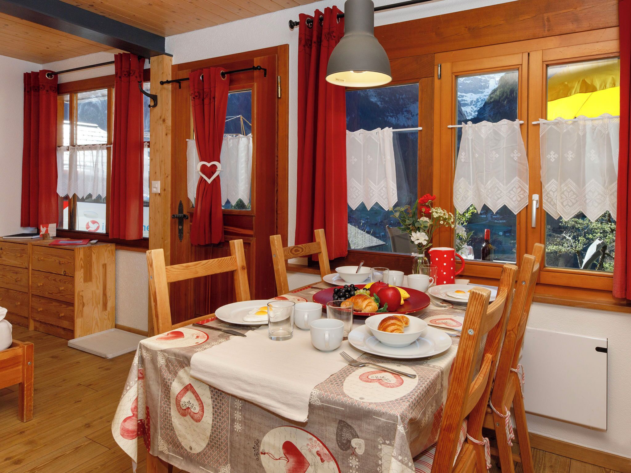 A dining area with a table set for breakfast, wooden furniture, and a view of a snowy landscape through the windows.