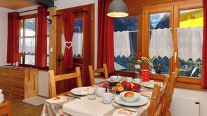 A dining area with a table set for breakfast, wooden furniture, and a view of a snowy landscape through the windows. - Chalet Almisräba by Interhome (Grindelwald)