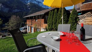 A table set outdoors with a mountain view, a yellow umbrella, and a bottle of wine. - Chalet Almisräba by Interhome (Grindelwald)