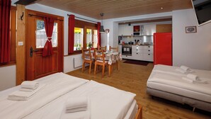 A hotel room with two beds, a dining table, chairs, a kitchen area, and a red wall. - Chalet Almisräba by Interhome (Grindelwald)