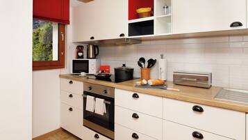 A modern kitchen with white cabinets, a wooden countertop, a stainless steel oven, and a red window blind.