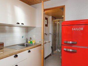 Een keuken met een spoelbak, kastjes, een aanrecht, een rode koelkast en een douchehoek.