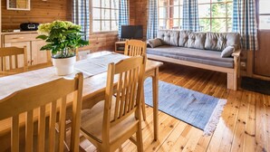 Un interior de cabaña acogedor con una mesa de comedor de madera, sillas, un sofá, un televisor y una planta en maceta.