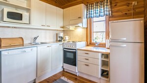 Una cocina compacta con armarios blancos, un microondas, un horno, un fregadero y un refrigerador.