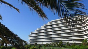 A modern multi-story hotel with a flat roof and horizontal lines, surrounded by well-maintained greenery and palm trees. - Les Terrasses du Levant by Interhome (Canet-Plage)
