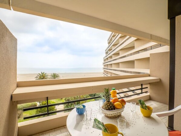A balcony with a table set for breakfast, overlooking a beach and a hotel building.