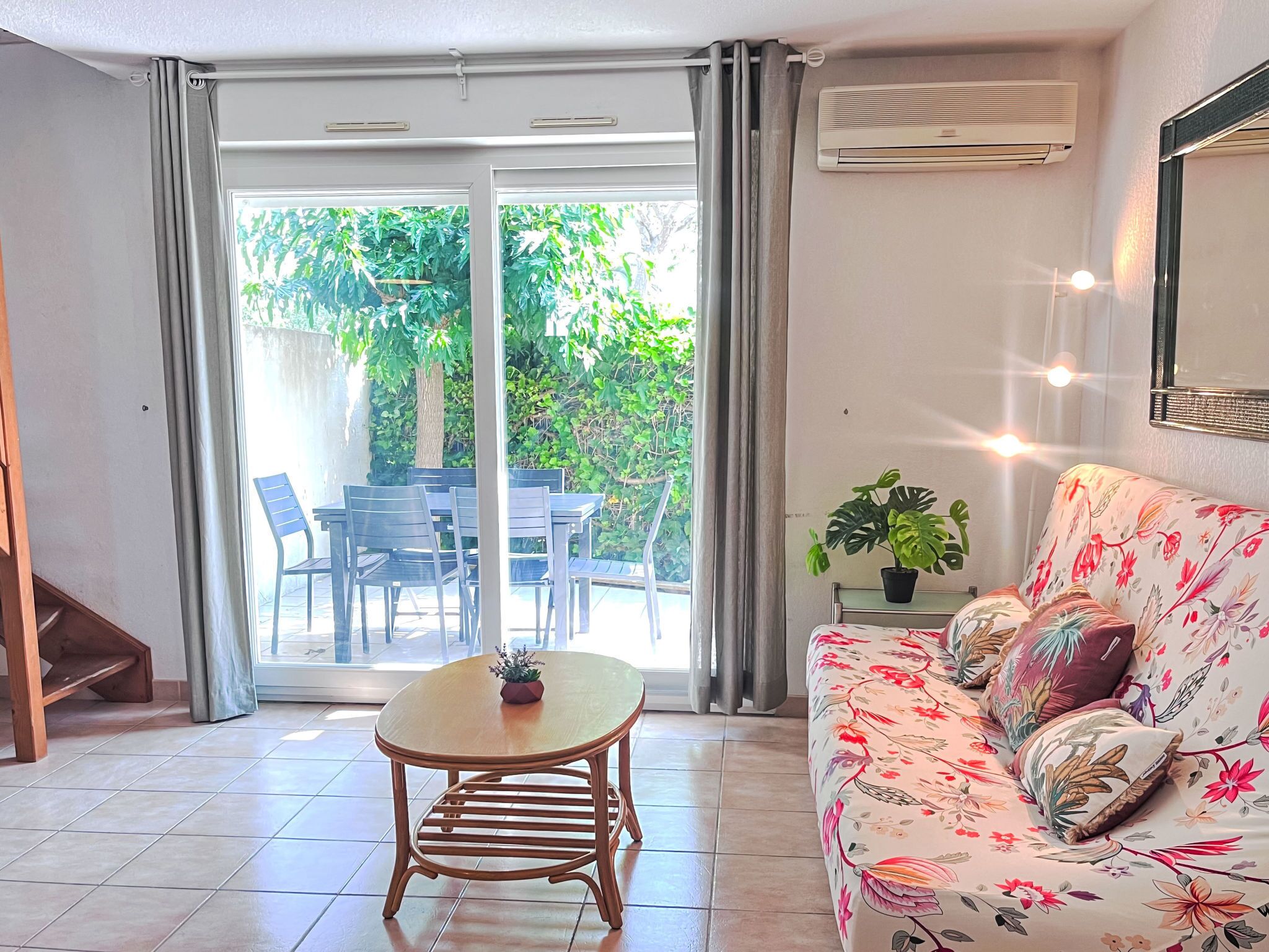 A living room with a sofa, a small table, and a chair. There is a sliding glass door leading to an outdoor area with a table and chairs.