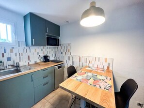 Una cocina compacta con armarios verde azulado, un microondas, un lavamanos y una mesa de comedor con sillas.
