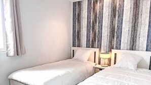 Ein Schlafzimmer mit zwei Einzelbetten, einem Holzkopfteil, einem Nachttisch mit Lampe und einem Fenster mit Vorhängen.