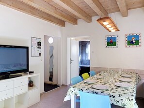 Un comedor con una mesa dispuesta para cuatro, un televisor sobre un mueble, y una puerta que da al baño.