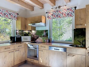 Une cuisine moderne avec des meubles en bois, un four encastré et une grande fenêtre donnant sur la forêt.