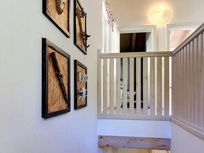 Una escalera con barandilla blanca, escalones de madera y un muro con obras enmarcadas.