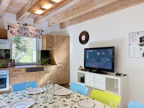 A modern kitchen with wooden cabinets, a dining table set for four, and a television mounted on the wall.