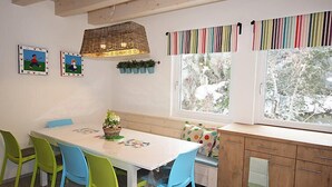 A dining area with a white table, colorful chairs, a bench, and a window with a view of trees. - am Arlberg by Interhome (Pettneu am Arlberg)