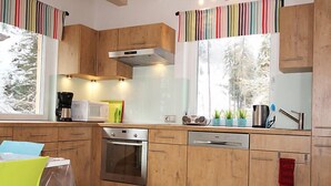 A modern kitchen with wooden cabinets, stainless steel appliances, and a window with a view of trees. - am Arlberg by Interhome (Pettneu am Arlberg)