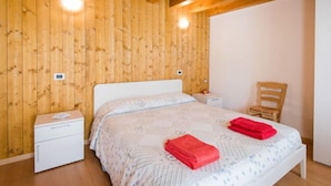 A wooden-paneled bedroom with a bed, nightstands, and a chair. - Albergo Diffuso - Cjasa Paron Cilli by Interhome (Barcis Lake)