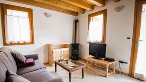 A living room with a sofa, a TV, a wooden cabinet, and a fireplace. - Albergo Diffuso - Cjasa Paron Cilli by Interhome (Barcis Lake)