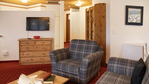 Ein gemütliches Wohnzimmer mit einem Karomuster-Sofa, einem passenden Sessel, einer Holzkommode und einem an der Wand montierten Fernseher.