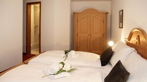 Ein ordentlich bezogenes Bett mit weißen Leinentüchern und ein Strauß weißer Blumen, ein hölzerner Kleiderschrank und ein gerahmtes Bild an der Wand.