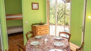 Quarto com uma cama de solteiro, mesa de jantar posta com pratos e copos, e vista para árvores através de uma porta de vidro.