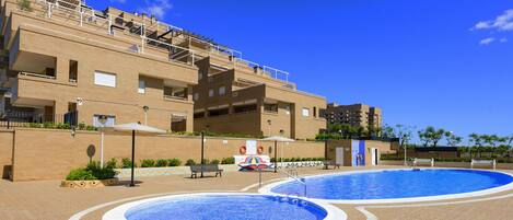 A pool area with two circular pools, a brick building with balconies, and a clear blue sky.
