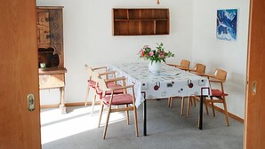 A dining area with a table set for six, surrounded by wooden chairs with red cushions. A vase with flowers is on the table, and a painting is on the wall. - Residenza Corallo by Interhome (Ascona)